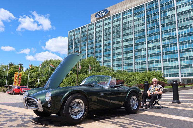 man sitting next to shelby cobra in front of Ford world headquarters