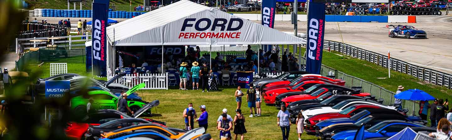 Ford mustang cars around a tent at a motorsports event.