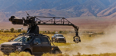 A movie camera mounted on a truck filming a Ford Raptor behind it
