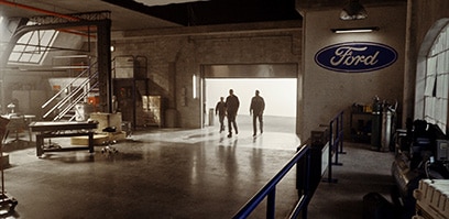 Wide angle shot of Ford Racing engineers walking into a garage backlit by daylight