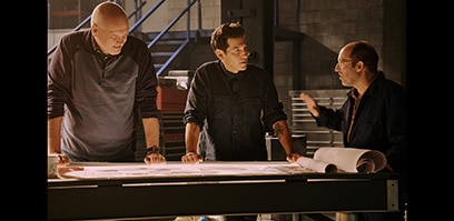Jon Bernthal and two engineers standing over engineering plans on a table