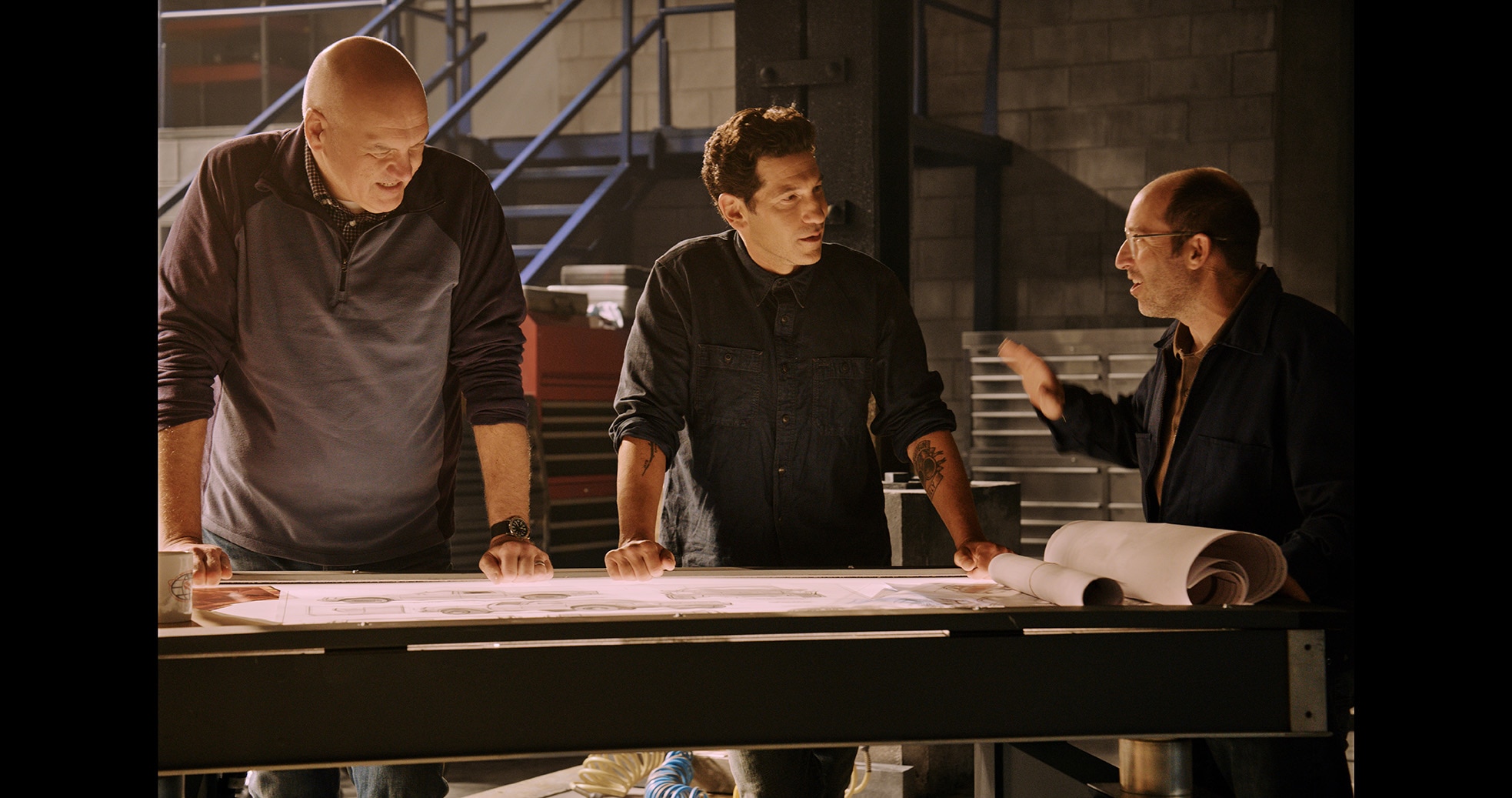 Jon Bernthal and two engineers standing over engineering plans on a table