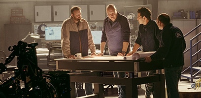 Wide angle of Jon Bernthal and the Ford Racing engineers standing over plans at a table