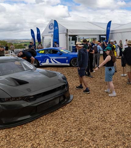 Ford mustang cars around a tent at a motorsports event.