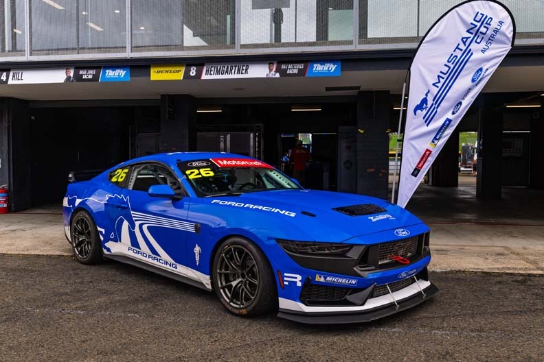 A blue and white race car with the number 13 crosses a checkered finish line on a race track