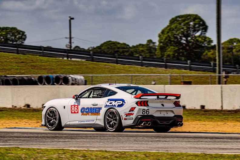 A blue and white race car with the number 13 crosses a checkered finish line on a race track