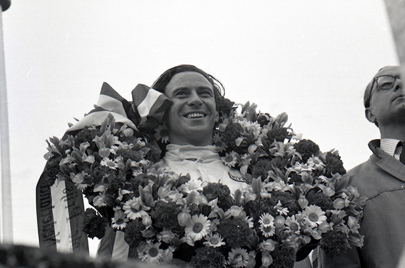 F1 Driver standing with circle of flowers around body in winners circle
